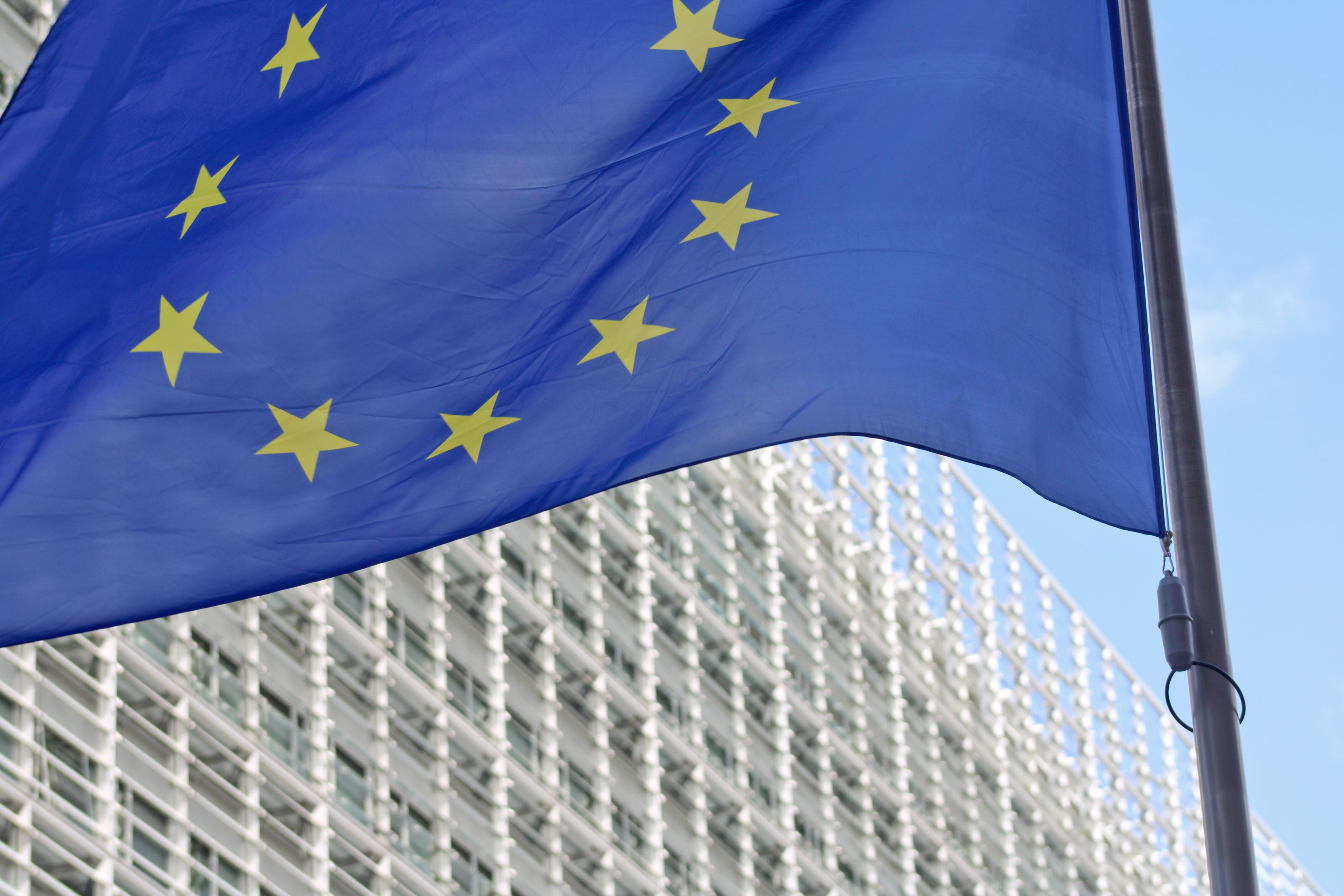 Decorative photo of the EU institutions headquarters in Brussels, place Schuman. It shows a close-up of the EU flag in front of the CE Berlaymont building, on a sunny day, September 2026